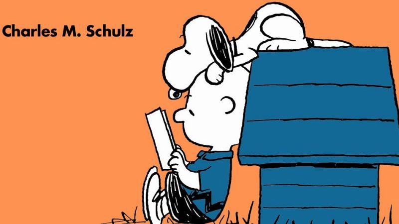 Carlitos Brown lee un libro cerca de la caseta azul de Snoopy, quien lo observa desde el techo.  Crédito a Charles M. Schulz en la parte superior.