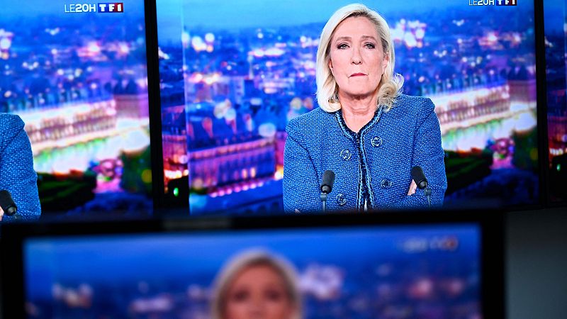 Marine Le Pen, en varias pantallas de TV, con chaqueta azul y brazos cruzados, sobre un fondo de ciudad nocturna iluminada.