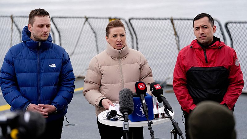 Conferencia de prensa al aire libre con tres personas; una mujer en el centro con un documento, y dos hombres a sus lados. Se ven micrófonos y una grabadora.