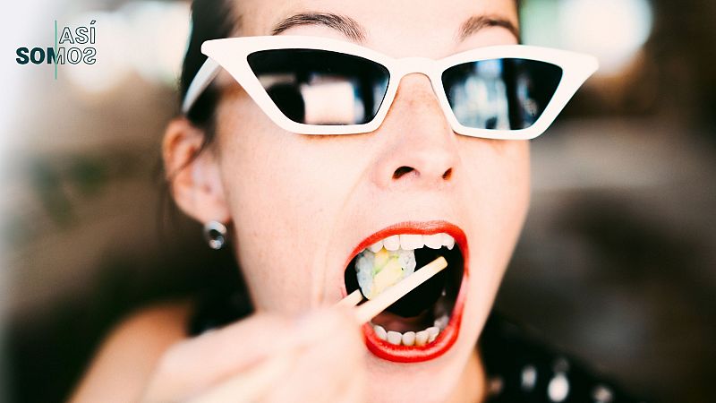 Mujer con gafas de sol blancas comiendo sushi con palillos; labios rojos; vestimenta oscura con lunares blancos.  Imagen relacionada con el programa de radio 'Así Somos'.