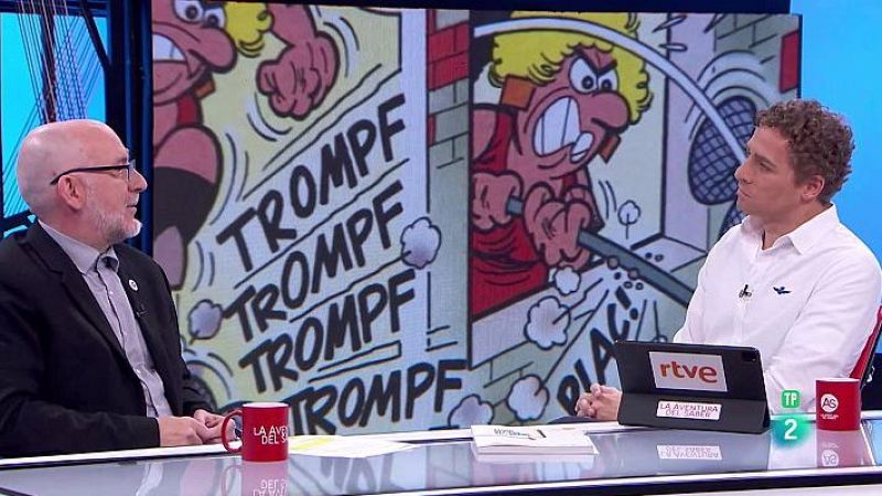 Alejandro Casasola y el presentador de 'La Aventura del Saber' sentados a una mesa con tazas y un portátil.  Detrás, viñeta de cómic con personaje rubio y la onomatopeya "TROMPF".