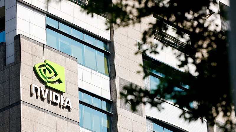 Logotipo de NVIDIA en la fachada de un edificio parcialmente oculto por hojas.  Imagen relacionada con problemas económicos.