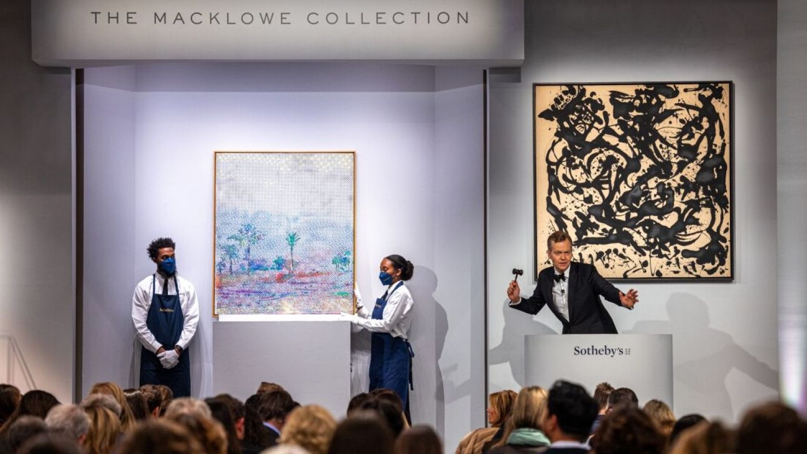 Subasta en Sotheby's: empleados presentan obra de arte con paisaje de palmeras, estilo puntillista/pixel art.  Pintura abstracta en blanco y negro visible en el fondo.