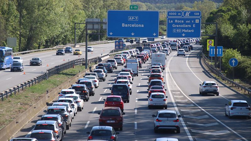Atasco en autopista con numerosos vehículos.  Señalización indica AP-7 Barcelona y otras salidas. Autobús circula en sentido contrario.