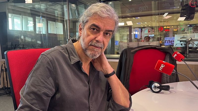 Escritor en estudio de radio RNE, sentado a una mesa con micrófonos y auriculares. Lleva camisa gris oscura.