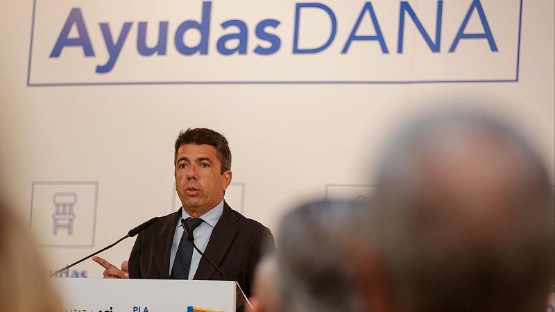 Presentación de ayudas DANA por el presidente de la Generalitat. Cartel con el texto "Ayudas DANA" visible al fondo.  Asistentes presentes.