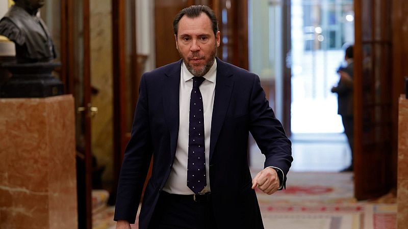 Ministro en traje oscuro caminando por pasillo del Congreso.  Expresión seria, camisa blanca y corbata oscura con puntos.  Estatua visible a su izquierda.