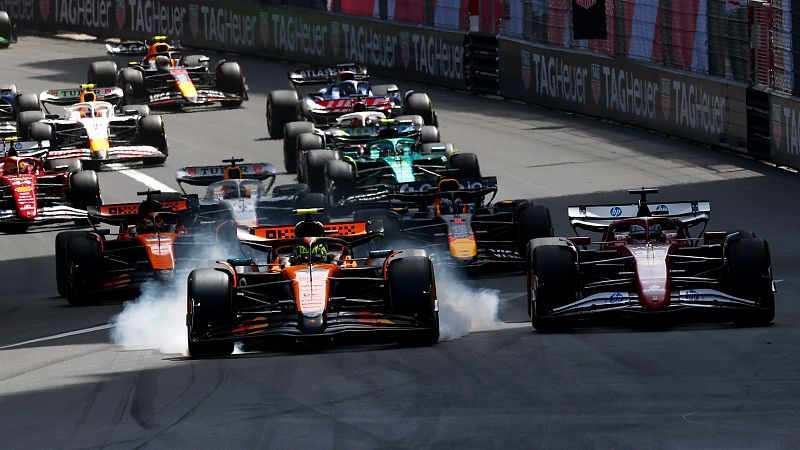 Intensa competición en una curva de F1 con coches muy juntos y humo de neumáticos.  Se aprecia el logo de Tag Heuer.