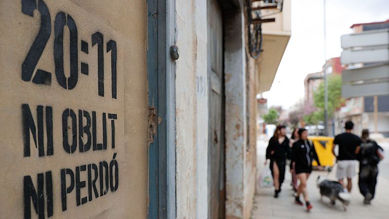 Graffiti en pared con la hora 20:11 y la frase "NI OBLIT NI PERDÓ" en mayúsculas. Personas caminando en segundo plano.