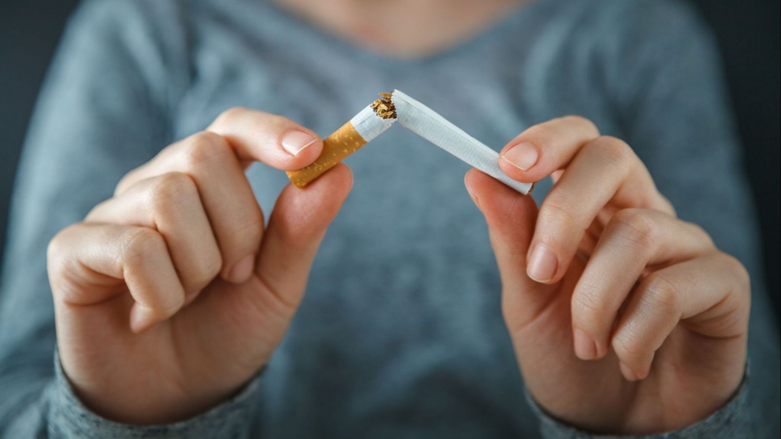 Manos partiendo un cigarrillo blanco por la mitad, simbolizando el abandono del hábito de fumar.