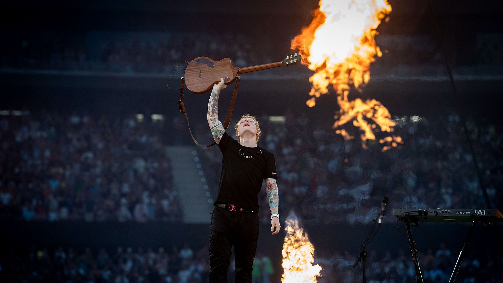 Concierto de Ed Sheeran en Madrid: El cantante, con guitarra en alto, ante una multitud y llamas en el escenario.