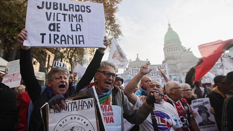 Marcha de jubilados en Buenos Aires contra el gobierno.  Carteles con mensajes de protesta, uno de ellos dice "JUBILADOS VICTIMA DE LA TIRANIA".  Rostros de enojo y frustración.