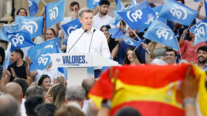 Discurso de Alberto Núñez Feijóo en un acto público con multitud y banderas del PP y de España.  El líder del partido habla tras un atril blanco con el logo del PP.
