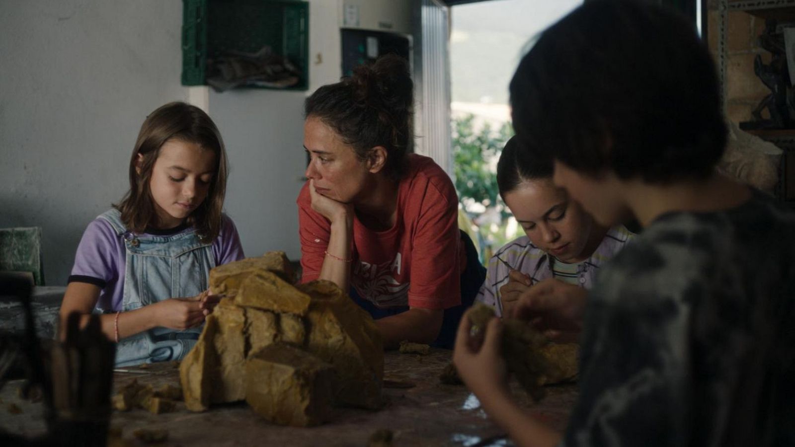 Mujer y tres niñas modelan arcilla en un ambiente hogareño y tranquilo.  Concentración en la creación de figuras de arcilla.