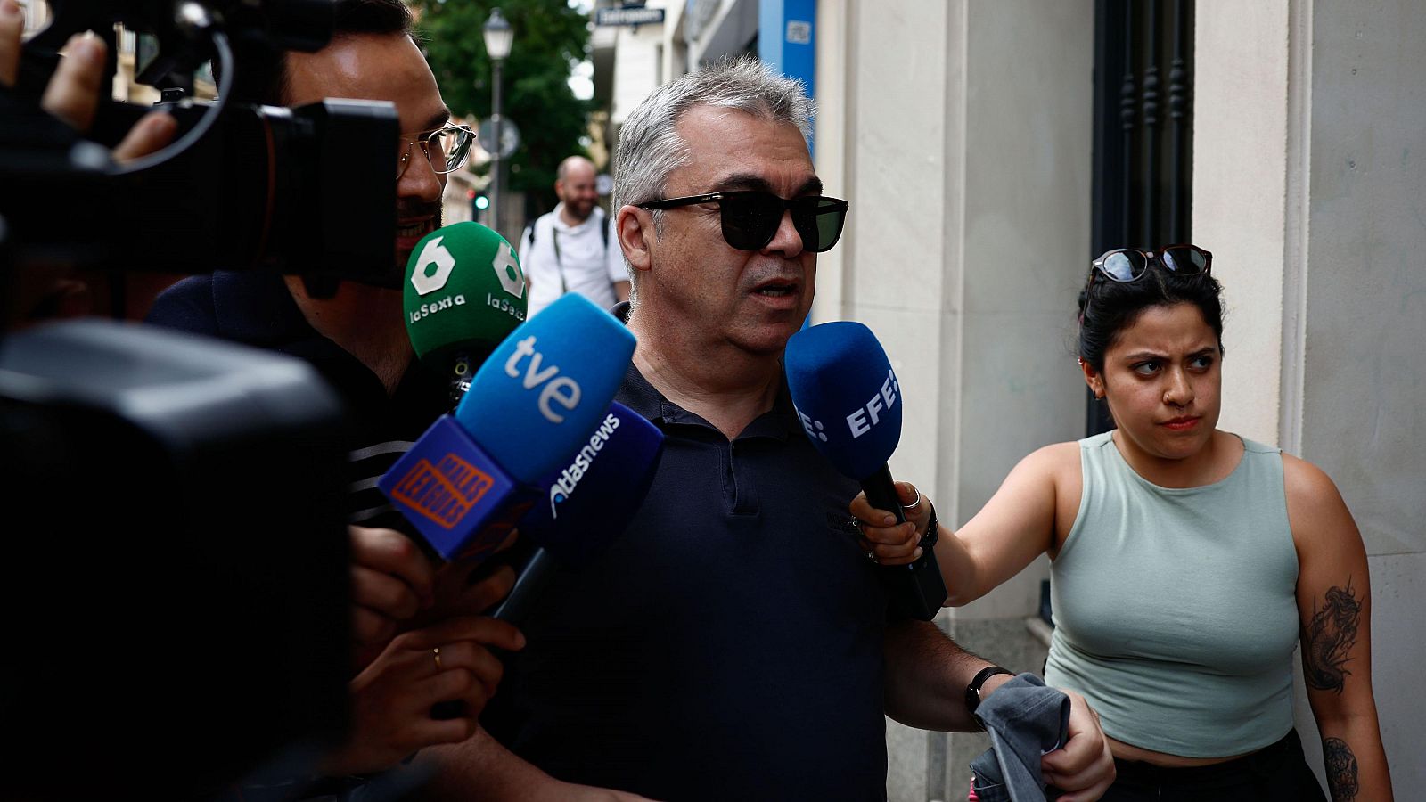 Entrevista a Santos Cerdán por varios periodistas con micrófonos de diferentes medios cerca de su domicilio. Una periodista le formula una pregunta seria.
