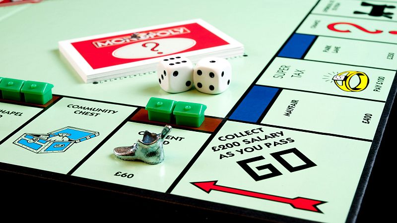 Tablero de Monopoly con dados (4 y 3), ficha de bota, casas, tarjetas y casillas como 'Mayfair' y 'Arca Comunal'.