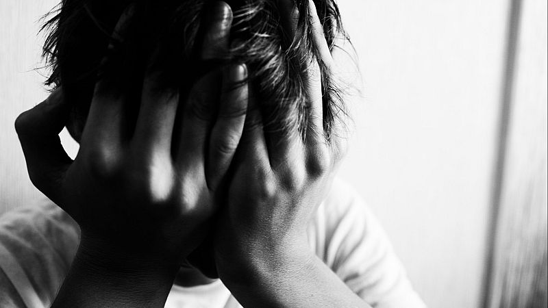 Imagen en blanco y negro de una persona con las manos sobre el rostro, mostrando una postura de profunda tristeza o angustia. Iluminación suave, contraste acentuado.