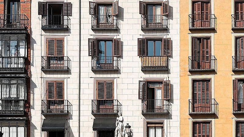 Tres edificis adossats, un de maó vermell i dos més moderns (crema i ocre), amb múltiples finestres, balcons i una estàtua a la base.