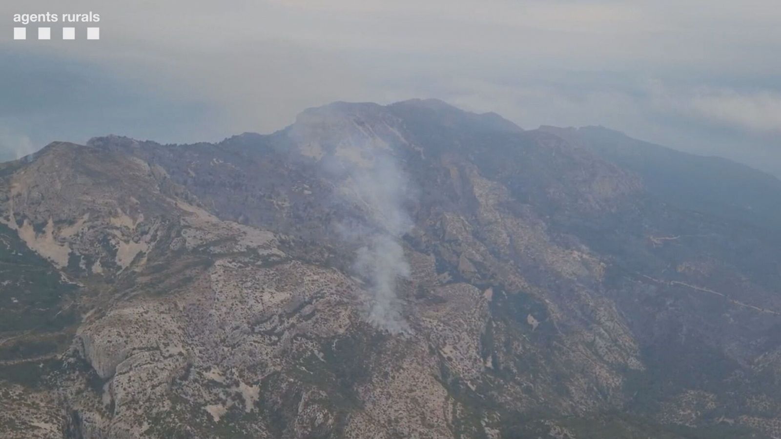 Incendio forestal en zona montañosa con abundante humo visible desde el aire.  Terreno rocoso y vegetación seca.