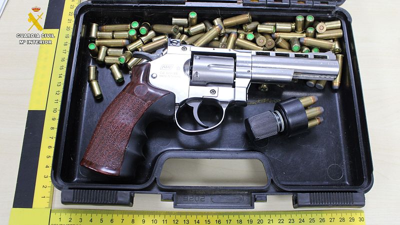 Revólver con empuñadura de madera, munición (puntas verdes) y cargador rápido en caja negra con regla métrica.  Logo Guardia Civil visible.