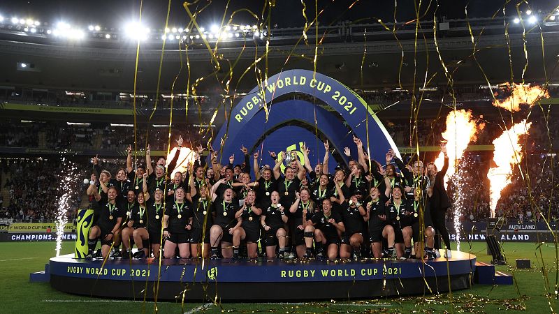 Jugadoras de rugby neozelandesas celebran victoria en podio con medallas, trofeo y fuegos artificiales.  Se lee "RUGBY WORLD CUP 2021" en el podio.