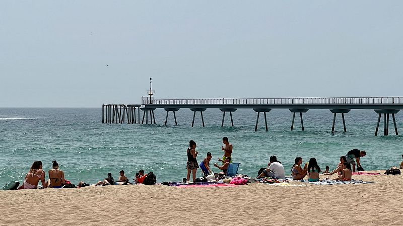 Gent a la platja de Badalona, amb el tram final del Pont del Petroli de fons | ACN: Jordi Pujolar