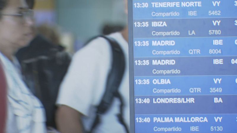 Panel de vuelos del Aeropuerto de Barcelona-El Prat mostrando horarios, destinos y códigos de aerolíneas.  Personas borrosas en segundo plano.
