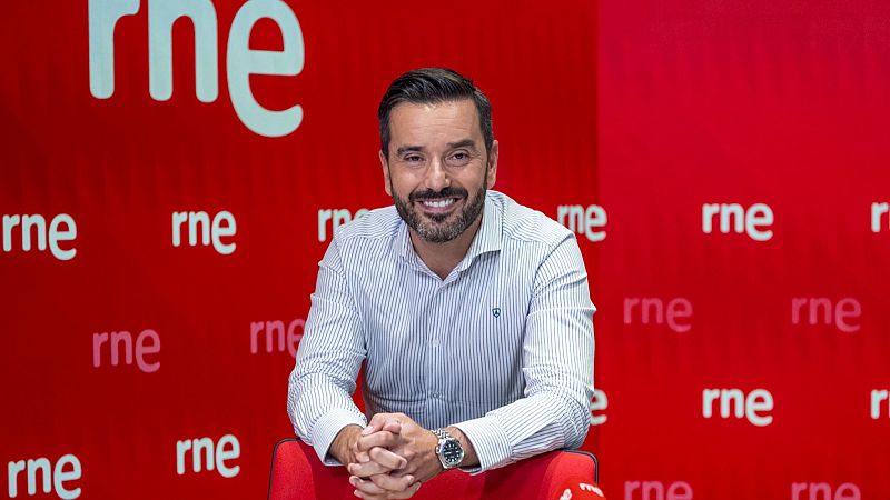 Presentador de RNE sentado, camisa a rayas, fondo rojo con logo repetido. Imagen promocional.