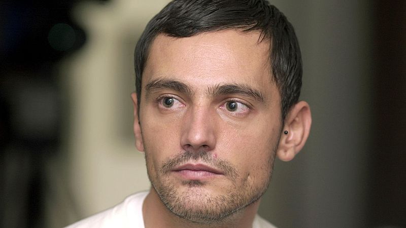 Retrato de un hombre con cabello y barba cortos, oscuro, y un pendiente; expresión seria, mirando a la izquierda; fondo oscuro y desenfocado.