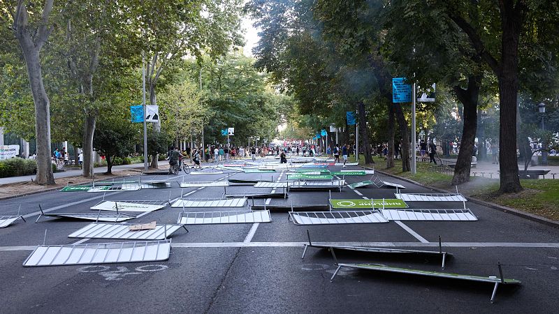 Vallas publicitarias metálicas derribadas tras una protesta.  Se observa humo o neblina y un grupo de personas al fondo.