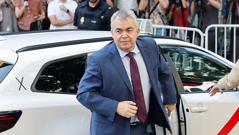 Un hombre de traje azul marino sale de un taxi blanco. Lleva camisa blanca y corbata granate. Al fondo, personas tras una valla y presencia policial.