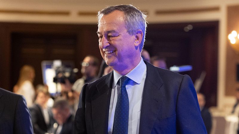 Imagen de Josep Oliu, presidente del Banco Sabadell, en un evento formal. Sonríe y mira hacia la izquierda, con traje azul oscuro y corbata azul con puntos blancos. Fondo con otras personas.