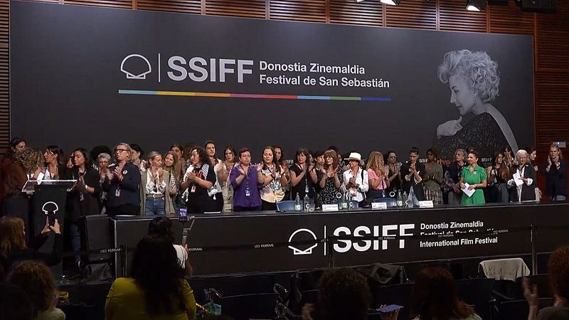 Grupo de mujeres aplaudiendo en un evento del Festival de Cine de San Sebastián, como protesta contra las violencias sexuales en la industria.  Se observa el logo del festival en un cartel.