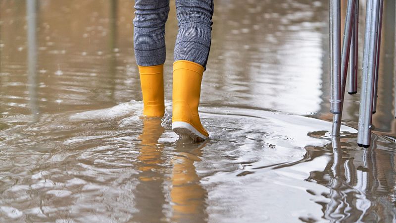 Una mujer caminando por la acera de una calle inundada por la lluvia