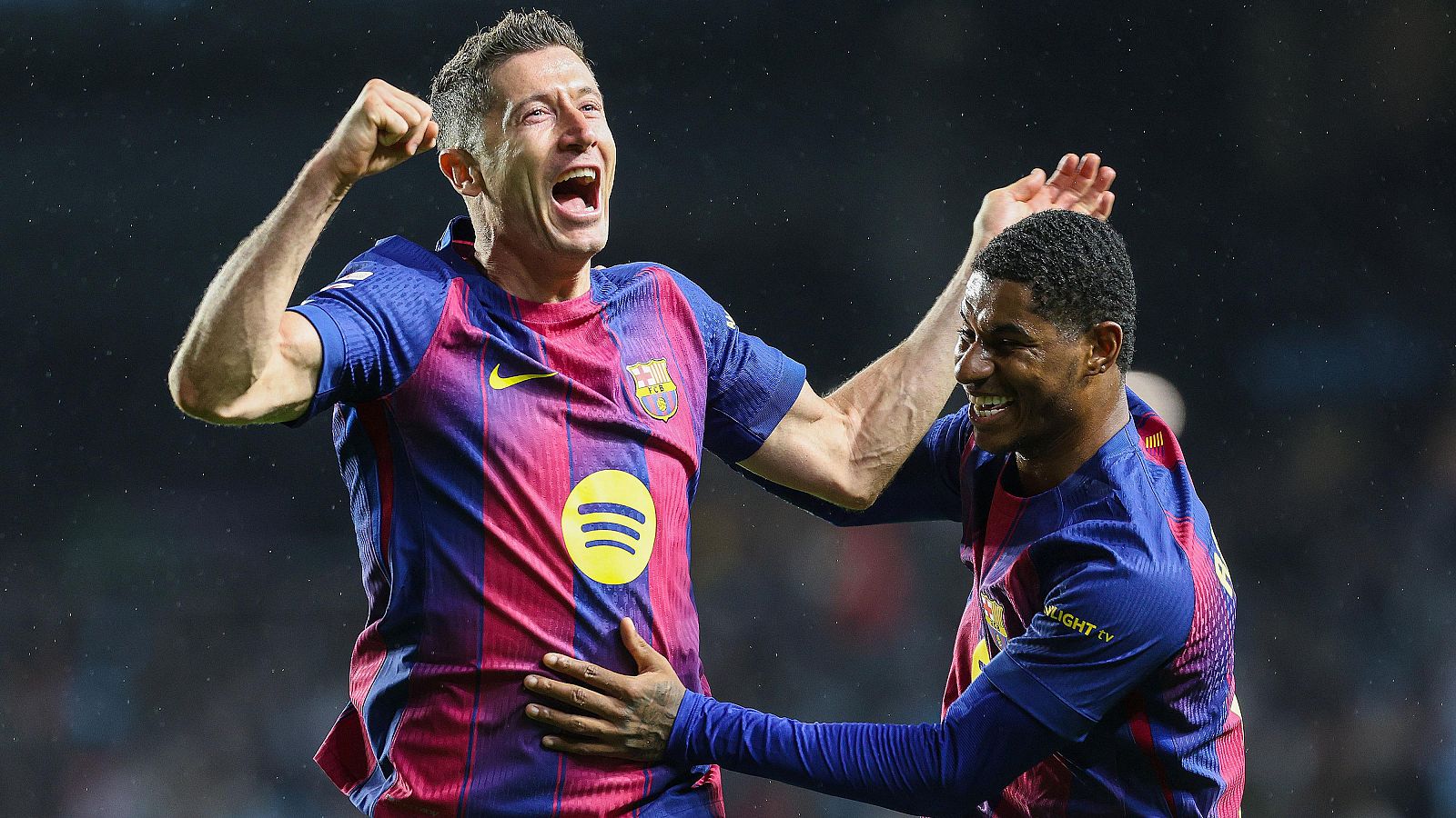 Dos futbolistas del Barcelona, con la camiseta azulgrana, celebran un gol en un estadio. Uno de ellos, con el puño en alto, grita, mientras que el otro lo abraza sonriendo.
