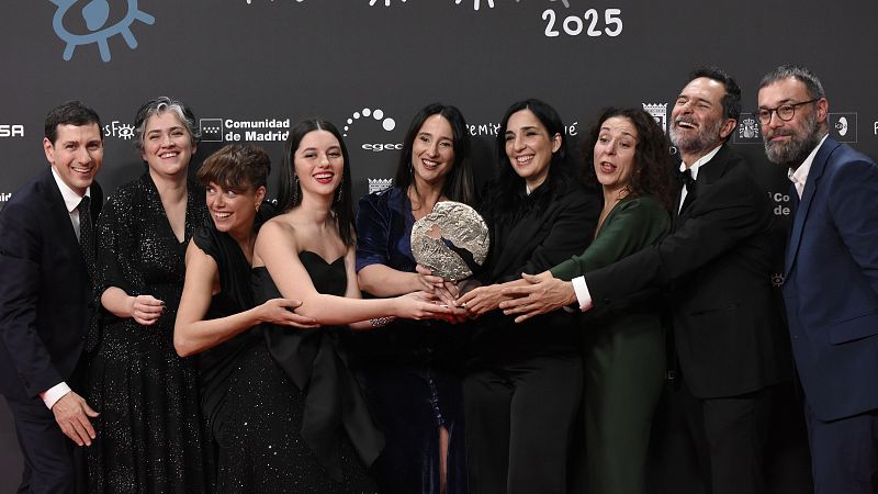 Nueve personas, vestidas elegantemente, sonríen sosteniendo un premio frente a un photocall con el logo de la Comunidad de Madrid. El grupo parece celebrar un logro.