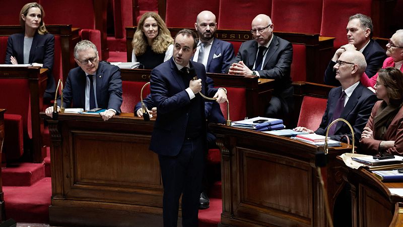 Sébastien Lecornu, el primer ministro, se encuentra en el parlamento, posiblemente hablando o gesticulando, rodeado de otros individuos sentados en escaños.