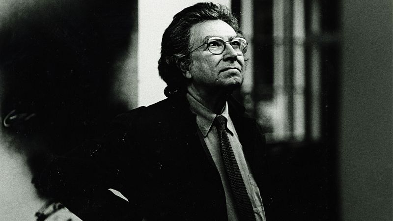 Retrato en blanco y negro de un hombre de mediana edad con gafas y corbata a rayas, mirando hacia arriba y a la derecha, en un interior con una ventana.