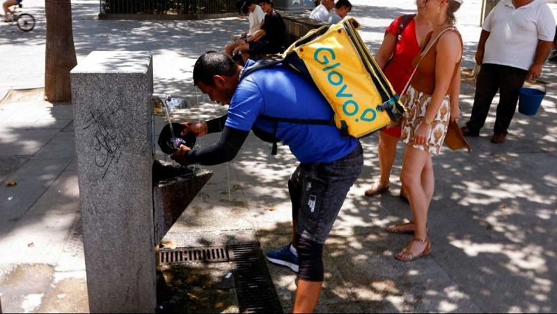 Un home mulla la gorra a l'aigua d'una font per refrescar-se.