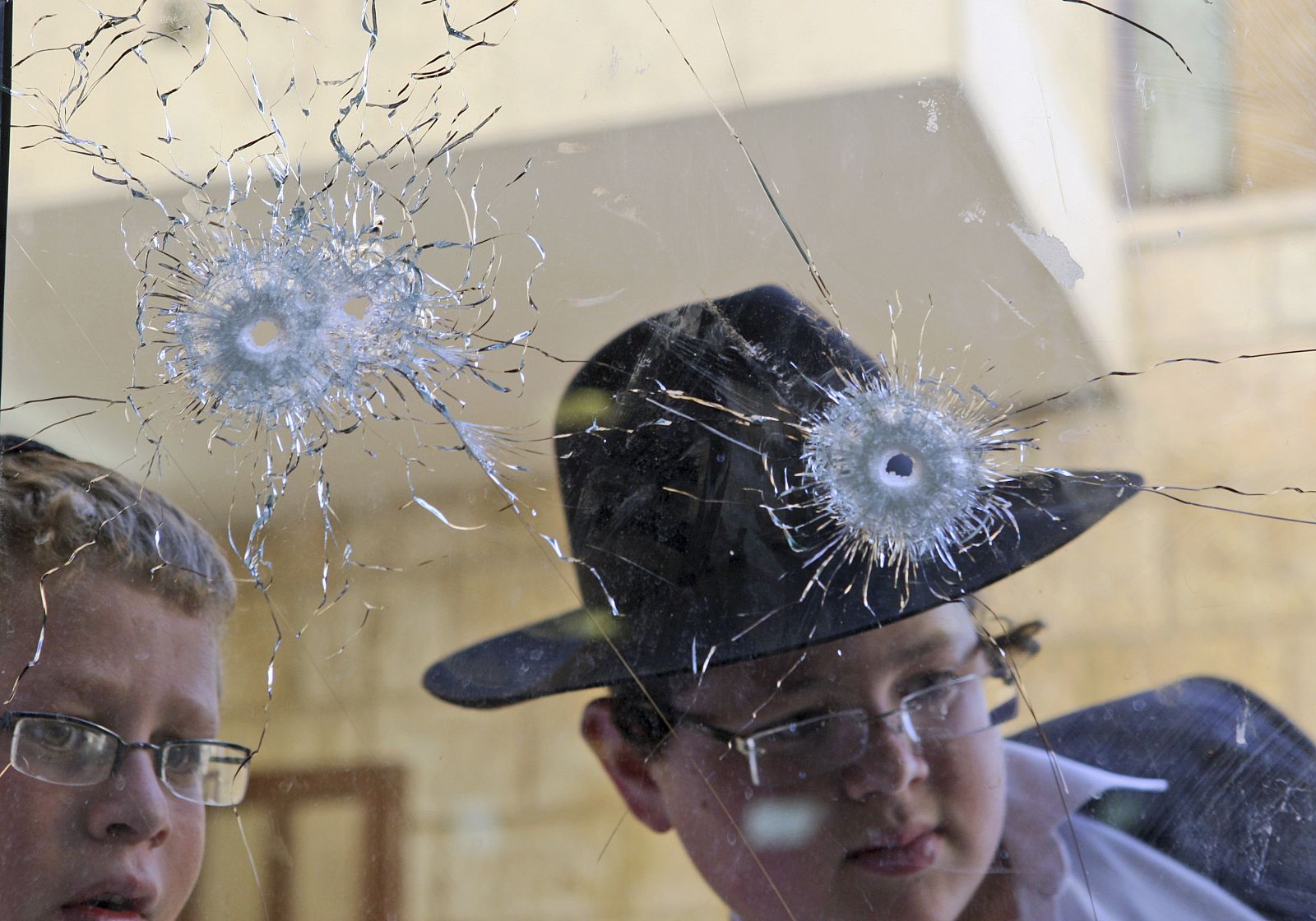 Dos niños miran una ventana con agujeros de bala tras el atentado en una escuela de Israel