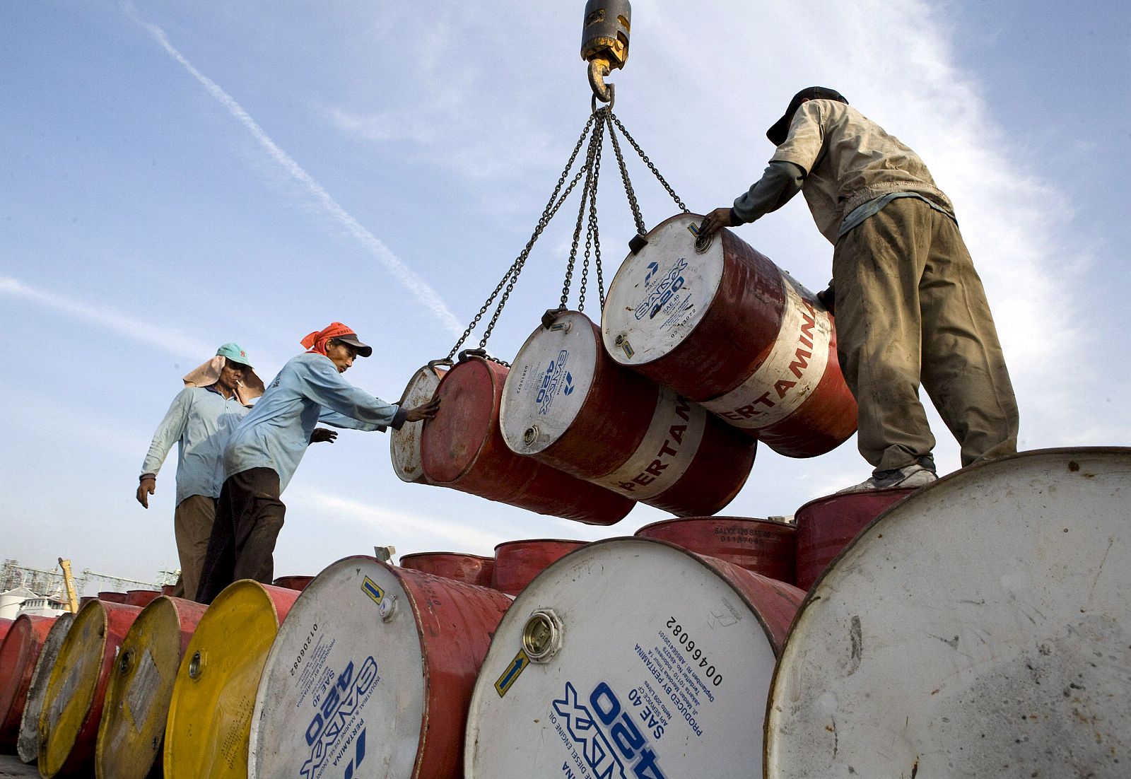 Operarios indonesios descargan barriles con petróleo