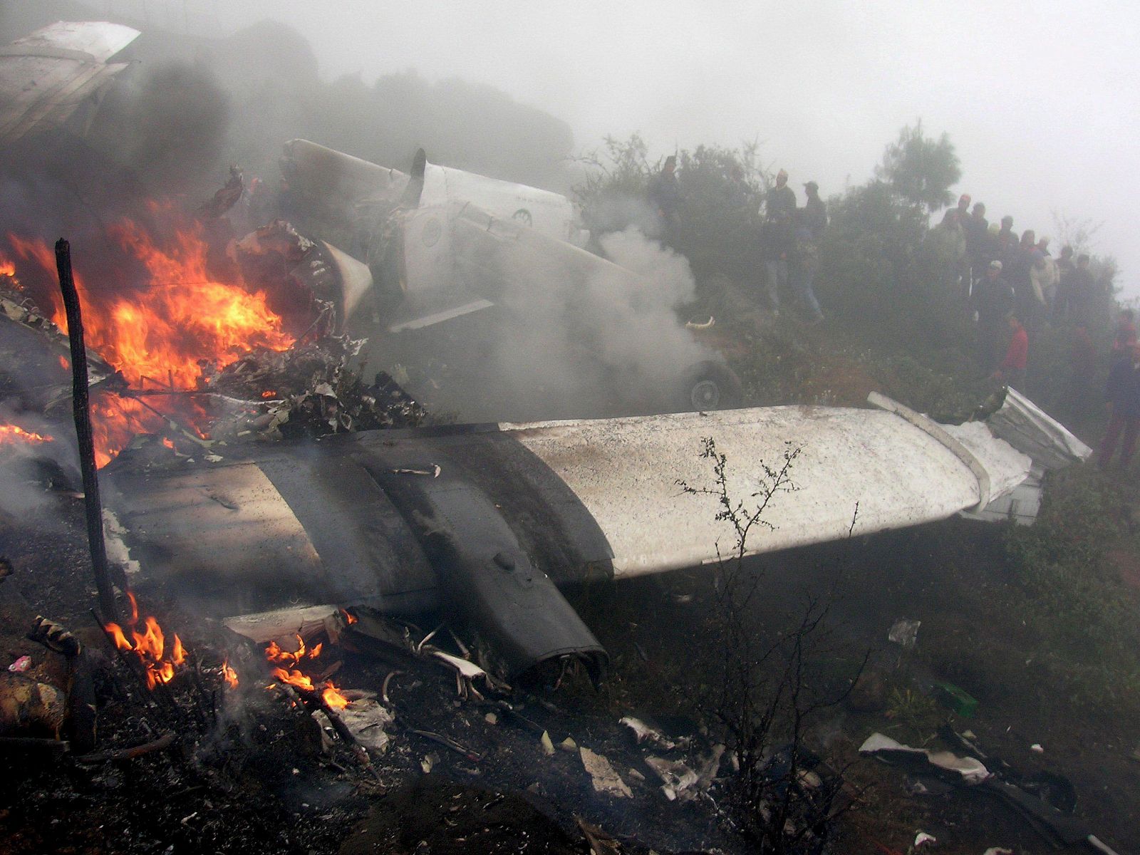 Un grupo de curiosos observa los restos aún en llamas de un avión de Yeti Airlines junto al aeropuerto de la remota localidad de Lukla.