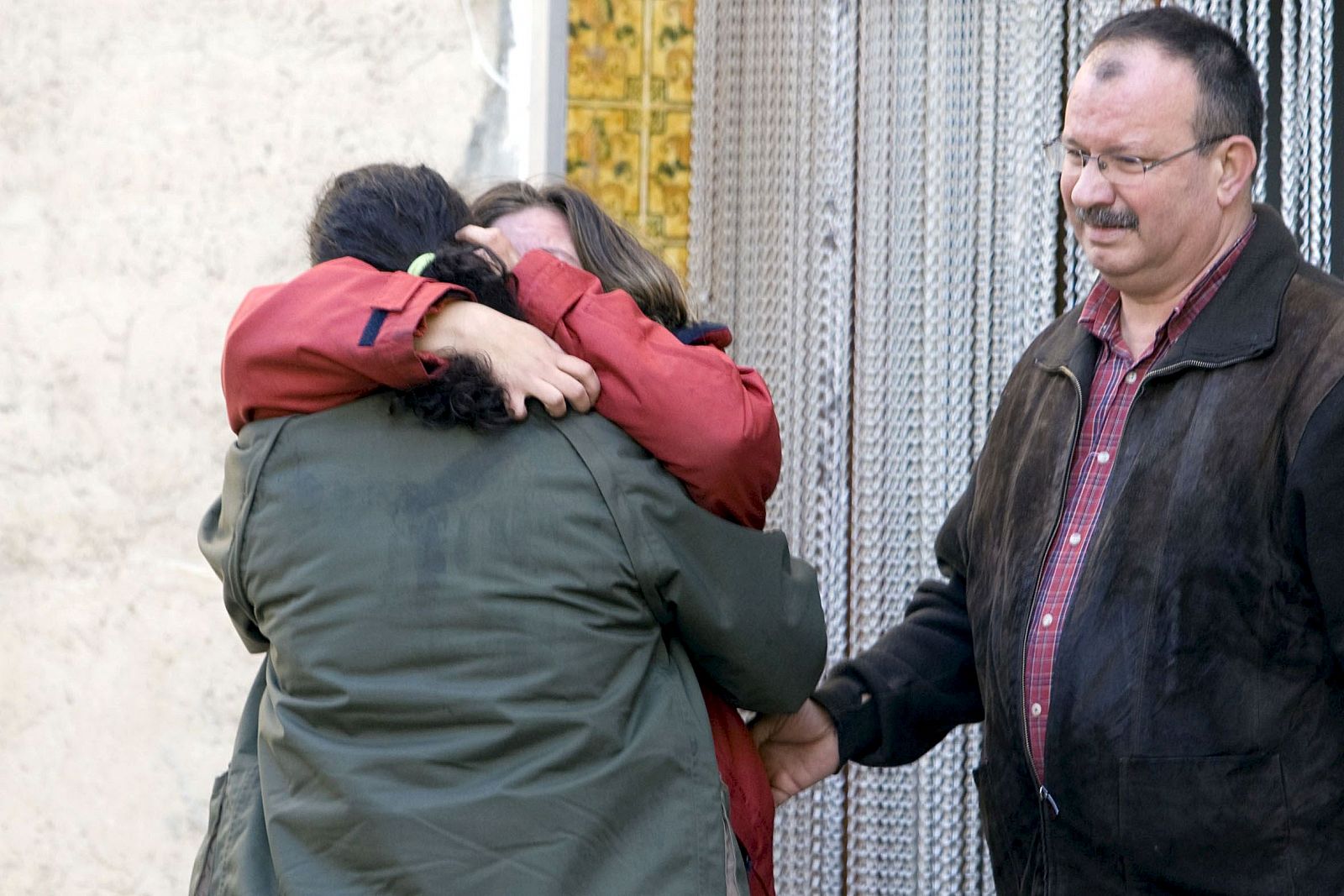 El padre y la madre, de rojo, del niño fallecido por un incendio producido en su habitación, a la puerta de la casa donde ha tenido lugar el suceso.