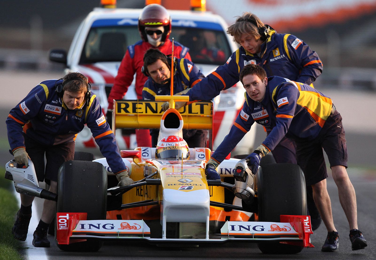 Varios mecánicos de Renault remolcan el coche de Fernando Alonso.