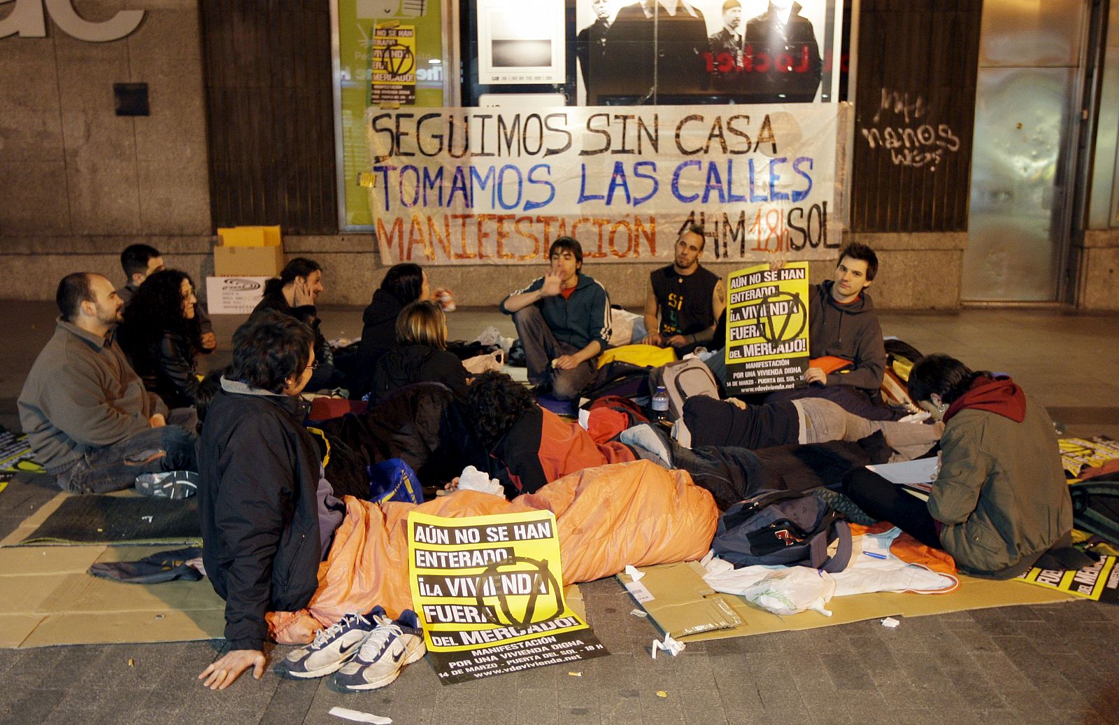 Jóvenes activistas de 'VdeVivienda' protagonizan una 'dormida' en la calle Preciados de Madrid, rodeados de pancartas en las que abogan por el "Alquiler Social Universal".