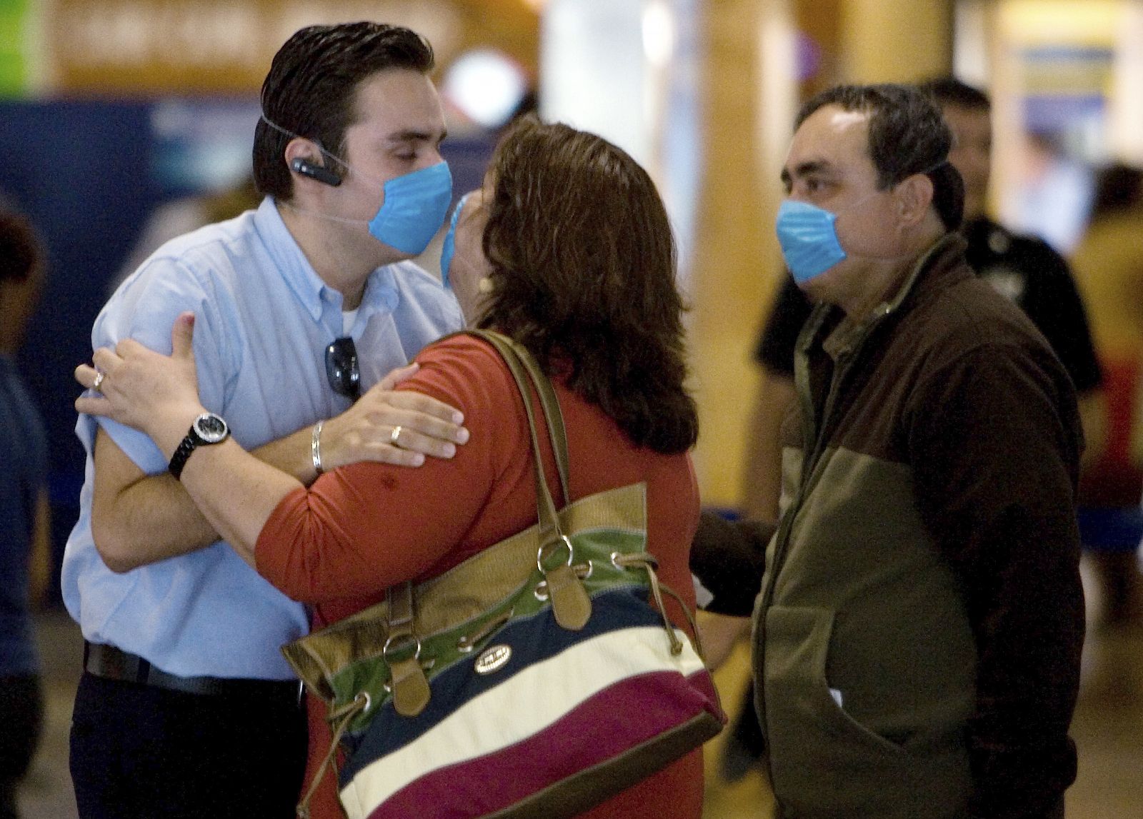 A couple wearing surgical masks kiss each other goodbye as the woman is about to board a plane at the international airport in Cancun, Mexico
