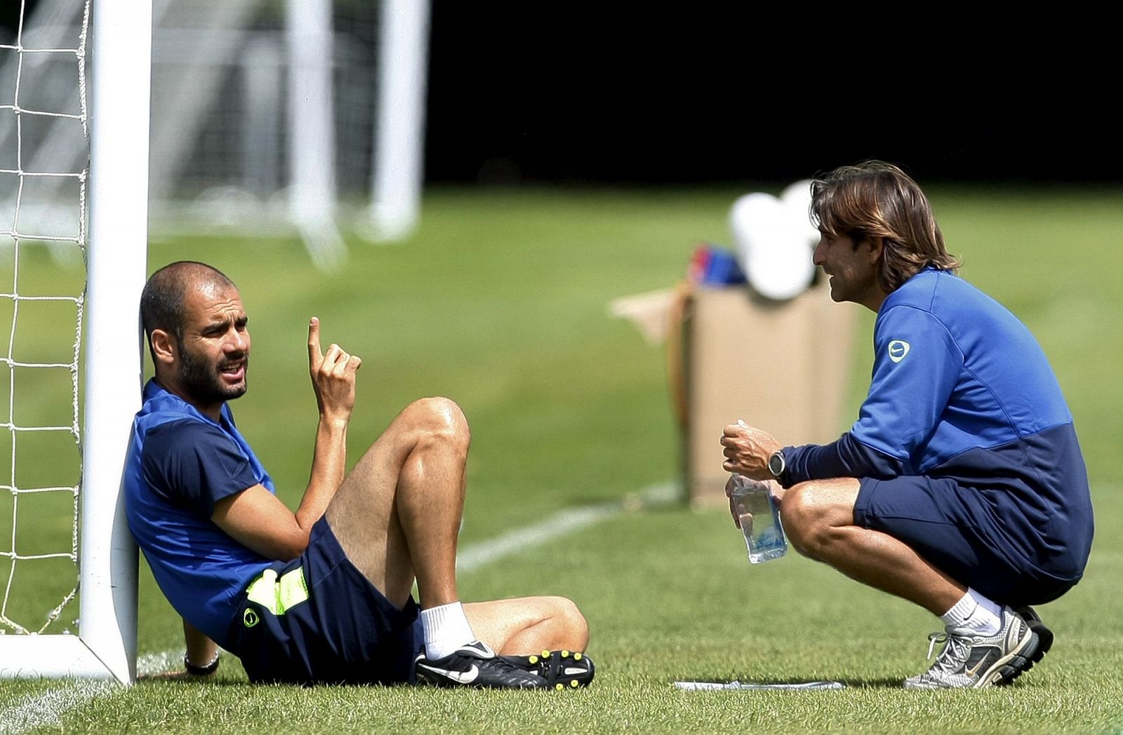 Guardiola habla con un miembro de su equipo téncico en el entrenamiento del Barça en Bisham