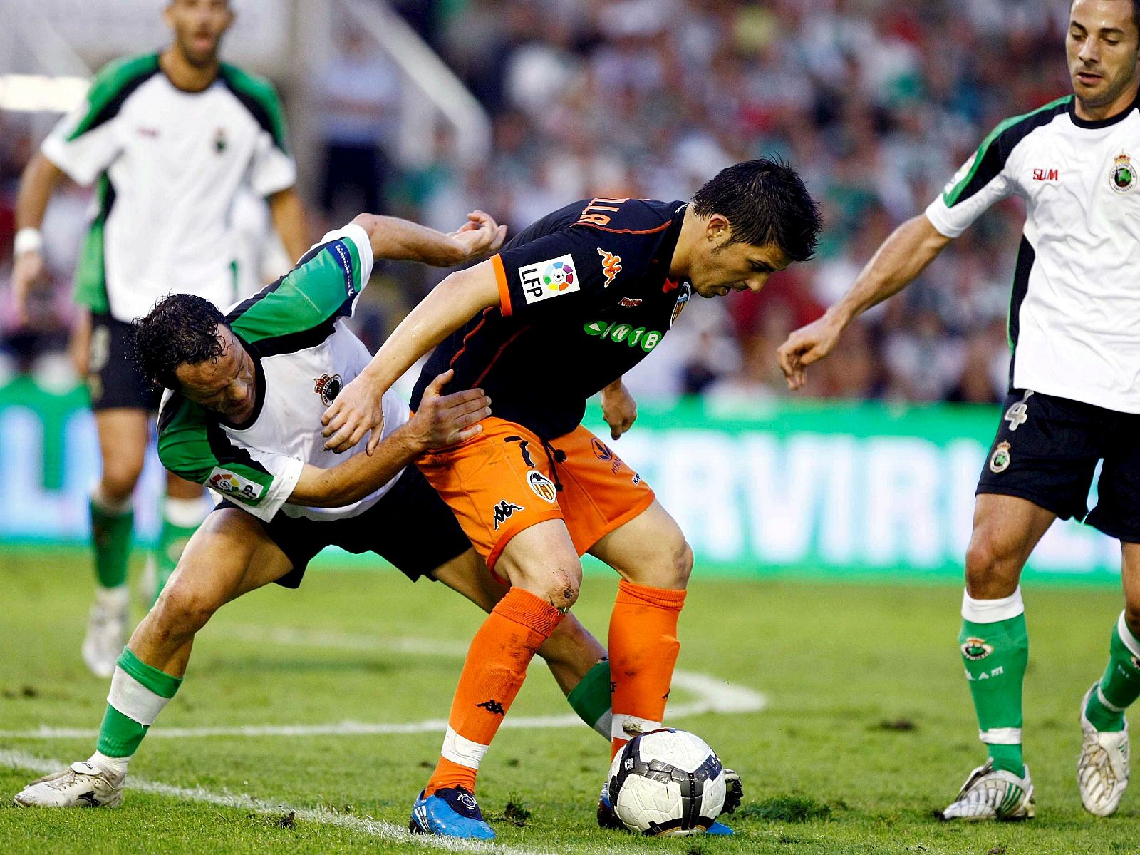 El delantero del Valencia David Villa controla la pelota ante la presión del defensa del Racing de Santander Pablo Pinillos y el centrocampista francés Mehdi Lacen.