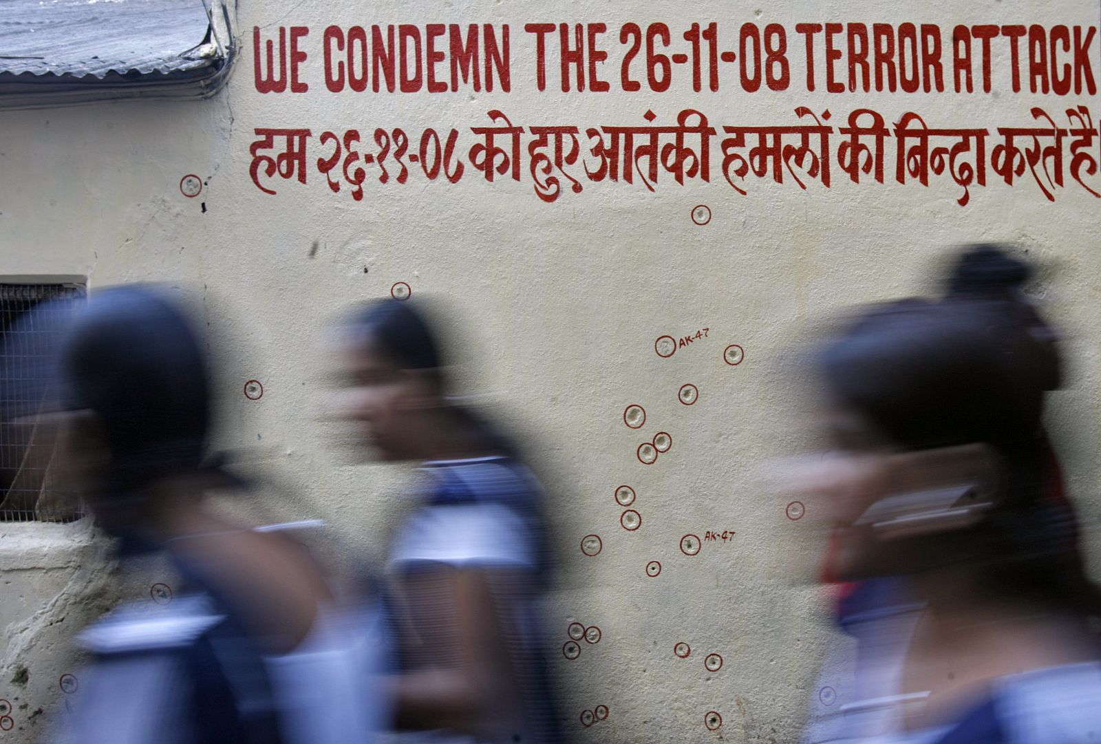 Unas escolares pasan junto a un muro agujereado por las balas durante la masabre de Bombay.