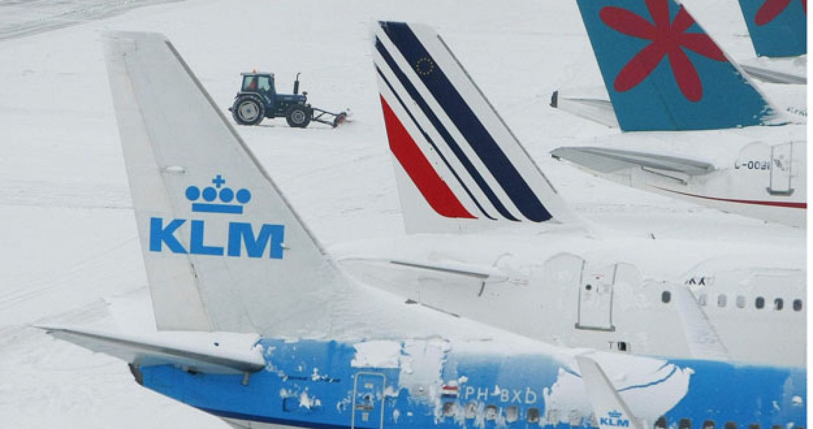 A tractor with a snow plough attached, clears snow between parked aircraft at Manchester Airport